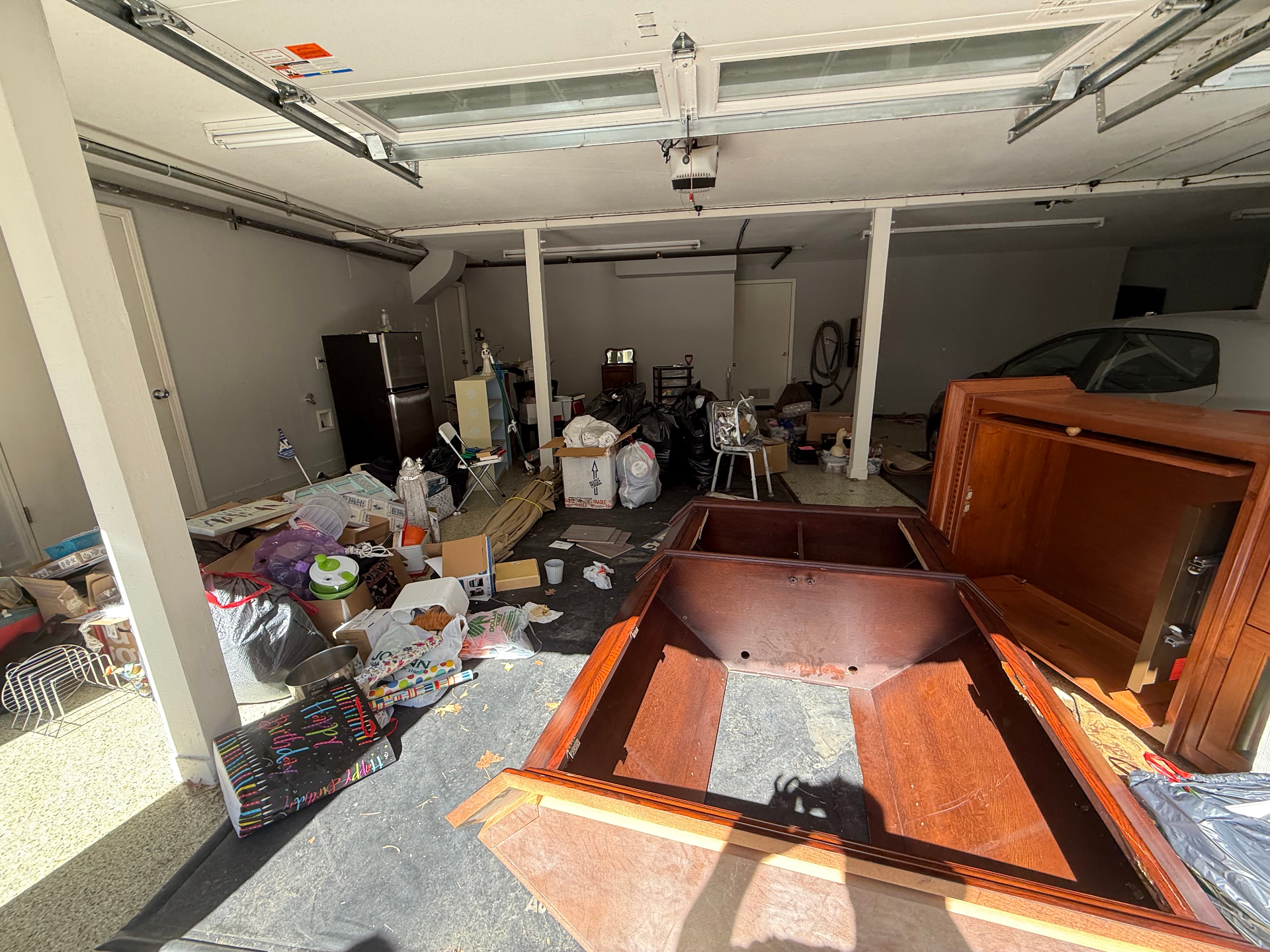 Cluttered garage filled with furniture, boxes, and bags before removal